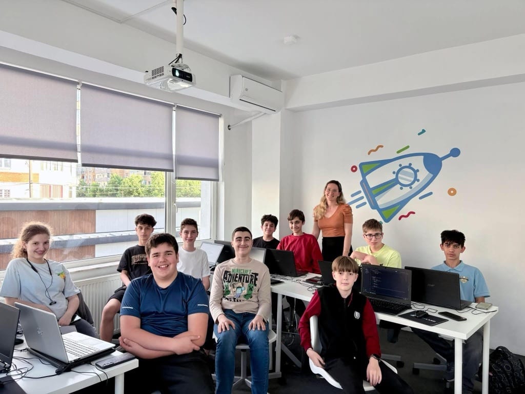 Grupă de adolescenți la un curs de programare Codeland, împreună cu profesoara, în sala de curs.