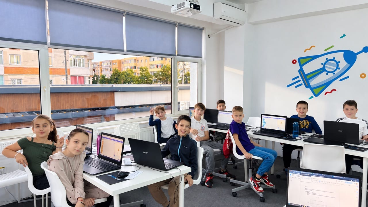 Copii la un curs de programare Codeland, lucrând la laptopuri în sala de curs din Pitești.