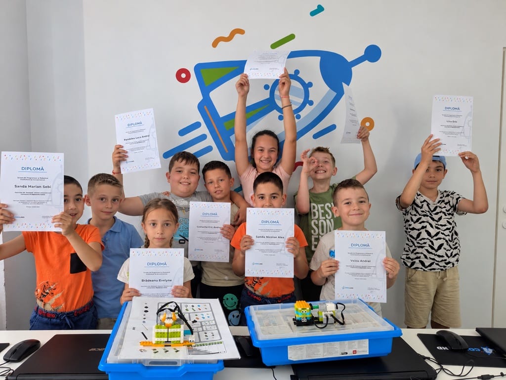 Copii de la Codeland ținând diplomele de absolvire, cu roboții LEGO construiți pe masă.