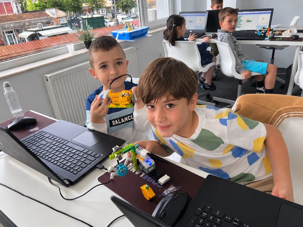 Doi copii la cursul de Robotică LEGO Codeland, arătând roboții construiți și programați de ei.
